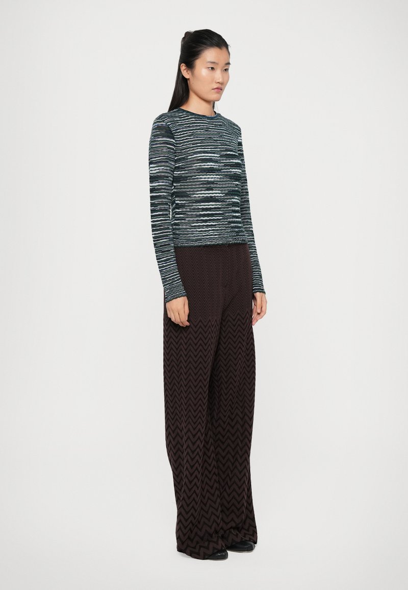 Gestreepte langemouwtop in marineblauw en grijs, gecombineerd met brede zigzag-geprinte broeken in bruin. Glad textuur, getailleerd silhouet.