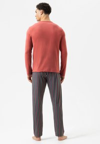 Langärmliges, korallenfarbenes Baumwolloberteil kombiniert mit mehrfarbigen, gestreiften Hosen mit vertikalen Linien in Grün, Pink und Blau.