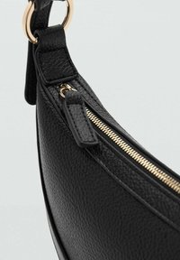 Crna torbica od teksturirane kože s zakrivljenim oblikom, sa zlatnim patentnim zatvaračem i akcentima od hardvera, te odvojivim remenom.