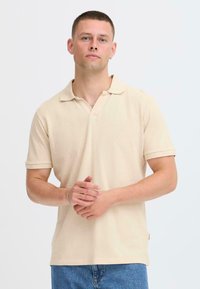 Polo beige avec un tissage texturé, manches courtes et col classique. Présente une broderie de logo discrète et une coupe décontractée.