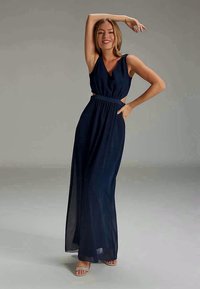 Mörkblå maxiklänning med skurna sidor, v-ringning och flödande kjol, tillverkad av ett lätt, genomskinligt tyg. Designad med en figursydd midja.