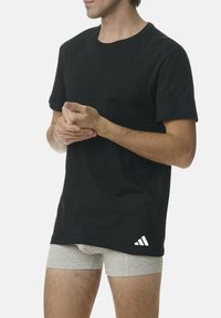 Czarny bawełniany T-shirt z okrągłym dekoltem i krótkimi rękawami, z białym logo w postaci trzech pasków na dolnym lewym boku. Model na zdjęciu nosi szare szorty.