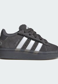 Black suede sneakers with three white serrated stripes. Features a grey rubber outsole and grey laces. Textured upper and classic design.