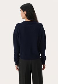 Pull en bleu marine avec une coupe ample, des poignets et un ourlet côtelés, présentant un col rond et un tissu doux et texturé.