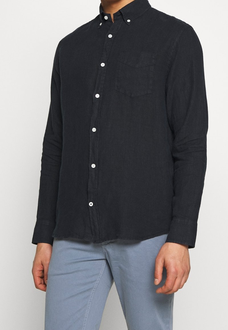 Dunkelblaues langärmliges Hemd aus Leinen, mit einem Knopfkragen, Brusttasche und weißen Knöpfen entlang der Knopfleiste.