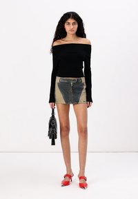 Sort off-shoulder ribbestrikket genser, denim miniskjørt med blå og beige paneler, røde høye hæler, og en svart håndveske.