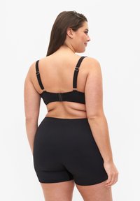 Schwarzes Unterwäsche-Set aus einem glatten, dehnbaren Stoff. Der BH hat verstellbare Träger und einen Hakenverschluss; kombiniert mit hoch taillierten Shorts.