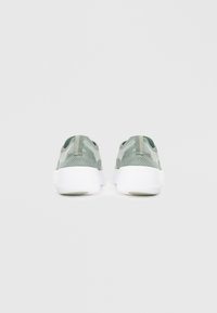 Grønne mesh-sneakers med en hvid sål, prydet med et struktureret mønster og en pull-tab bagpå for nemt på- og aftagning.