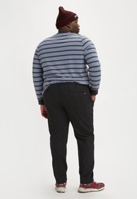 Blauw-wit gestreepte shirt met lange mouwen, zwarte broek, rode sneakers en een bordeaux gekleurde gebreide muts. Gedetailleerde stiksels op de broek, casual pasvorm.