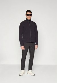 Melna vilnas jaka ar rāvējslēdzēja priekšpusi, kopā ar melnām biksēm un baltām sporta kurpēm. Modelis valkā lielas melnas saulesbrilles. Vienkāršs, piegulošs dizains.