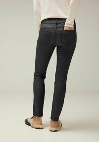 Jean slim noir avec une texture lisse et taille mi-haute, comportant deux poches arrière et un design ajusté, associés à des chaussures slip-on en fourrure.