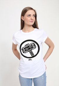 Hvid t-shirt med korte ærmer med et sort grafisk design af en stiliseret hammer inden for en cirkulær kant, sat mod en ensfarvet baggrund.