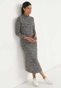 Zwart bloemen midi-jurk met lange mouwen en hoge halslijn, met een getailleerde bodice en een uitlopende onderkant, gecombineerd met witte sneakers.