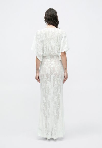 Pikk valge pitskleit, millel on lühikesed, laiad varrukad ja lillemustrid. Poolläbipaistev tekstuur, istuv vöökoht, põrandapikkusega disain, ilma täiendavate detailideta.