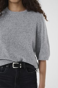 Maglioncino grigio chiaro a maniche corte in morbido tessuto peloso abbinato a jeans neri a vita alta, fissati con una cintura nera con fibbia argentata.