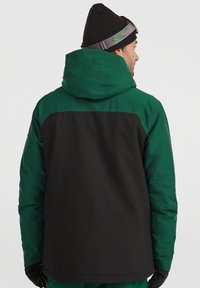 Grøn og sort udendørs jakke med en stor hætte, tekstureret stof og justerbare lukninger, der har et sort bagpanel og handsker.