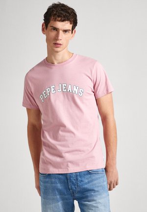 Camiseta de algodón rosa con el texto "PEPE JEANS" en blanco en forma de arco. Mangas cortas, cuello redondo, corte relajado. Combinada con jeans de mezclilla azul claro.