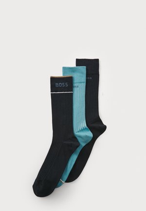 Three pairs of socks: one dark blue, one teal with vertical stripes, and one black, featuring ribbed texture and logo at the cuff.
