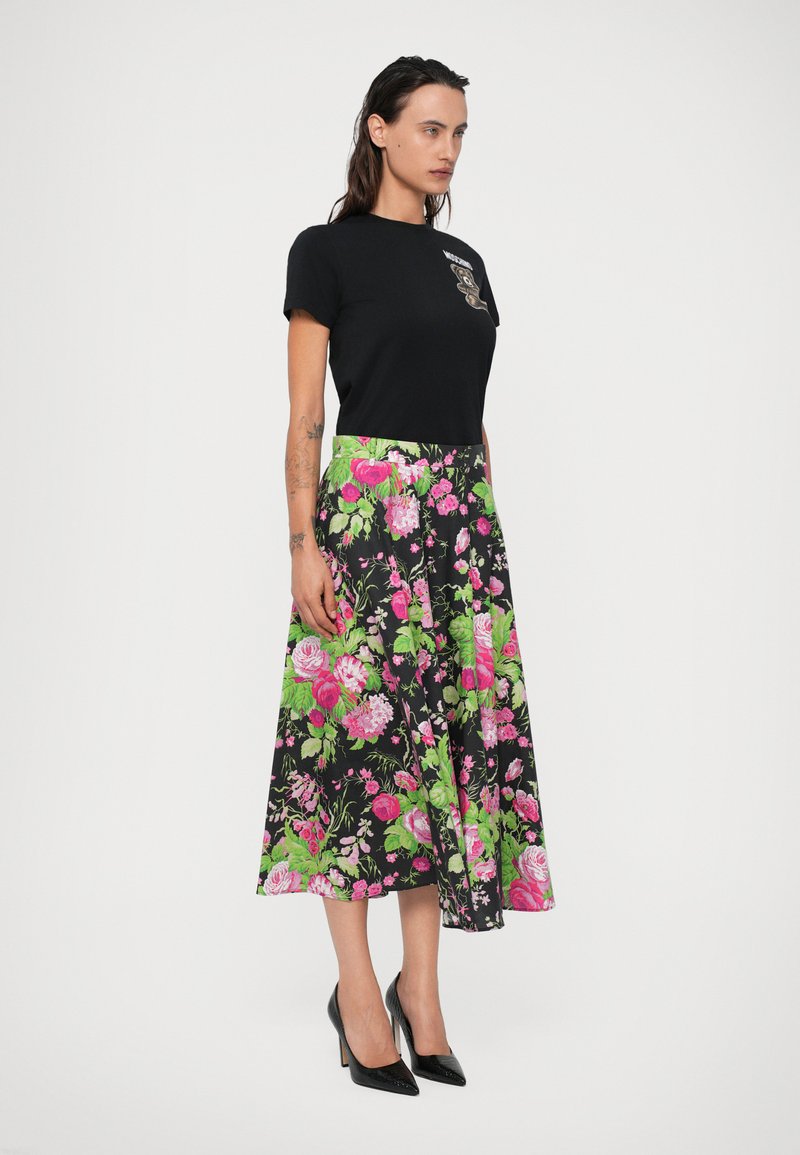 Sort kortærmet top med A-line nederdel mønstret med blomster, der har pink roser og grønne blade på en sort baggrund. Sorte højhælede sko.