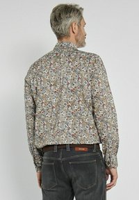 Koszula w kwiatowy wzór na beżowym tle, z długimi rękawami i kołnierzykiem. Posiada luźny krój, mankiety na guziki oraz miękką fakturę materiału.