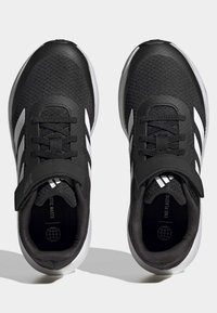 Zapatos deportivos negros con parte superior de textil, diseño de tres franjas blancas, puntera reforzada y una correa de Velcro, con una suela acolchada.