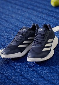 Granatowe buty sportowe z teksturowanej syntetycznej cholewki, białymi pasami i gumową podeszwą. Posiadają sznurowanie i wyściełany kołnierz dla zwiększenia komfortu.