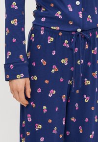 Top e calças de pijama azul-marinho com um padrão floral. O tecido é macio e com uma textura suave. Apresenta um fecho de botão e uma cinta ajustável.