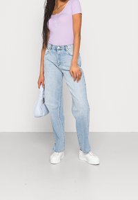 Ljuslila räfflad topp med korta ärmar, matchad med ljusblå raka jeans och vita plattformssneakers, hållande en ljusblå väska.