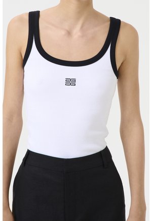 White ribbed tank top with black trim and small centered black logo, worn tucked into high-waisted black pants on a person.