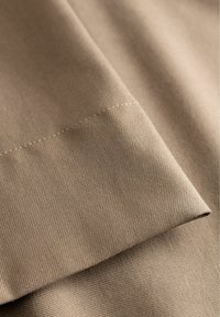 Beżowa tkanina o fakturowanej powierzchni, z diagonalnym prążkowaniem i czystym, prostym szwem na krawędziach. Miękki wygląd, matowe wykończenie.