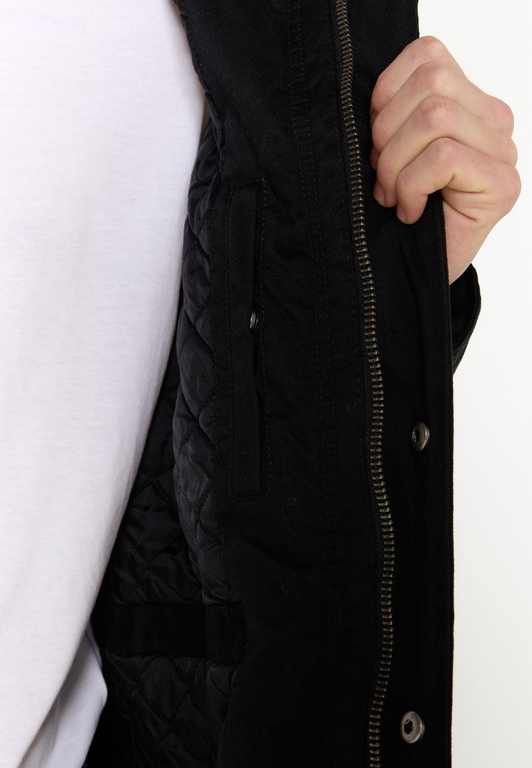 Veste noire avec un intérieur matelassé, dotée d'une fermeture éclair et d'accents à boutons-pression. Comprend une poche latérale à l'intérieur.