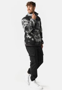 Suéter difuso con patrón en negro y gris y un alto cuello, combinado con pantalones cargo negros y zapatillas blancas. Un look casual y con textura.