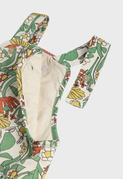 Sangle avec bouton ouvert sur tissu à motif floral, montrant la doublure intérieure beige du vêtement.