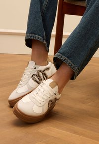 Weiße Turnschuhe mit strukturiertem Obermaterial, Akzent im Leopardenmuster und einer braunen Gummisohle. Tragen mit hochgekrempelten blauen Jeans.