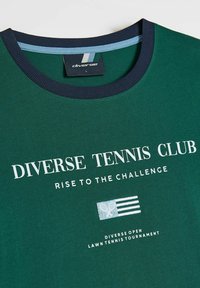 Zielona bawełniana koszulka z granatowym ściągaczem. Na przodzie znajduje się biały napis "DIVERSE TENNIS CLUB" oraz logo z krzyżującymi się rakietami i paskami.