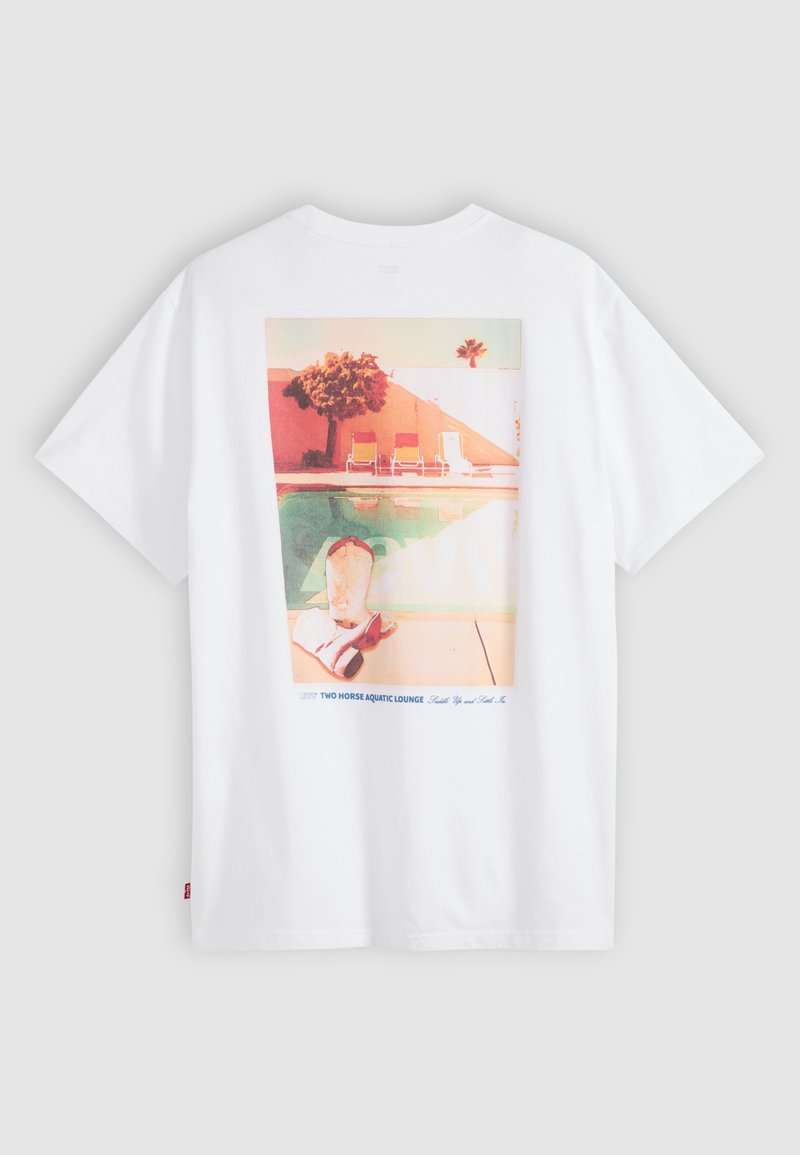 Weißes T-Shirt mit einer bunten Grafik von Poolstühlen, einem Pool, einem Baum und Cowboy-Stiefeln am Beckenrand.