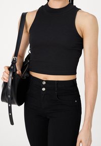 Top corto negro de canalé con cuello alto, combinado con jeans negros de tiro alto que presentan detalles de botones y bolsillos, acompañado de un bolso negro.