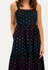 Sleeveless black dress featuring a tiered skirt, adorned with multi-colored polka dots in pink, green, blue, and orange.