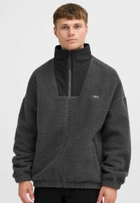 Fleece-pullover i mørkegrå med høj krave, halvlynlås foran og firkantet åbning. Har et lille "ISOLID" logo på brystet.