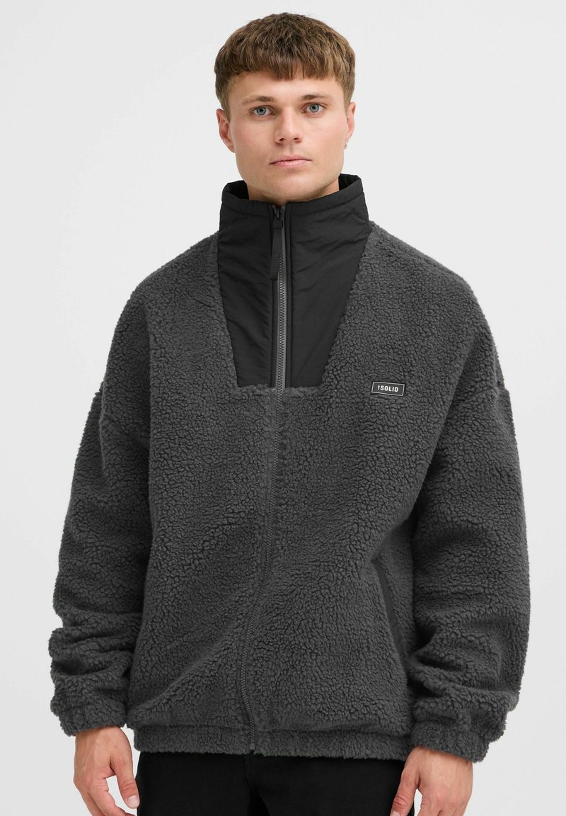 Fleece-pullover i mørkegrå med høj krave, halvlynlås foran og firkantet åbning. Har et lille "ISOLID" logo på brystet.