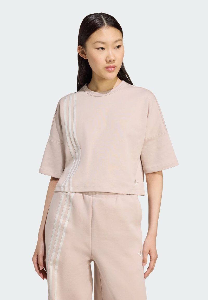 Svijetloružičasta skraćena majica s kratkim rukavima, s tri vertikalne pruge u svijetloplavoj boji s lijeve strane i malim logotipom.