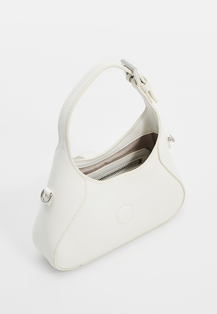 Sac à main en simili cuir blanc avec un design structuré, une courte poignée et un compartiment zippé. Présente un accent circulaire et des garnitures en argent.