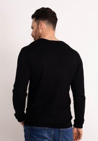 Maglione nero a maniche lunghe con collo a giro, polsini a coste e una texture liscia, abbinato a jeans blu, visto da dietro.