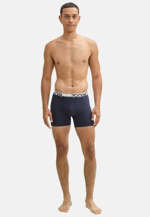 Boxer-briefs bleu marine avec une ceinture élastique arborant des accents de logo blancs. Texture de tissu lisse, longueur mi-cuisse, design ajusté.