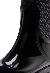 Botte de pluie noire brillante avec partie supérieure en tissu à motif et détail de bordure noire.