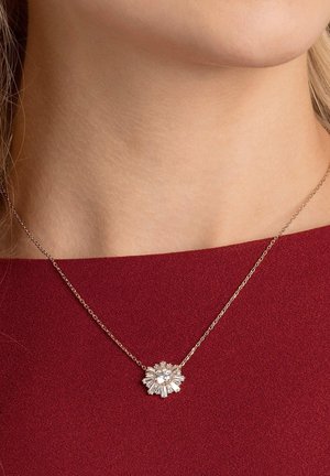 Collier en chaîne dorée avec un pendentif en forme de fleur orné de plusieurs pierres transparentes, présentant différentes tailles de taille et une surface texturée.