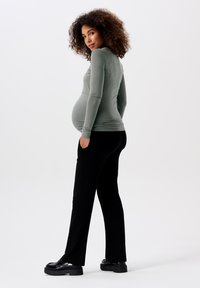 Langsleeve, aansluitend top in gedempt groen, gecombineerd met zwarte, losse broek. Model draagt stevige zwarte platform schoenen, haar in zachte krullen.