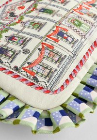 Dekoratyvinis pagalvėlė su spausdinta namų raštu ryškiomis spalvomis. Ji turi voliūrinį kraštą su žaliu ir mėlynu languotu raštu.