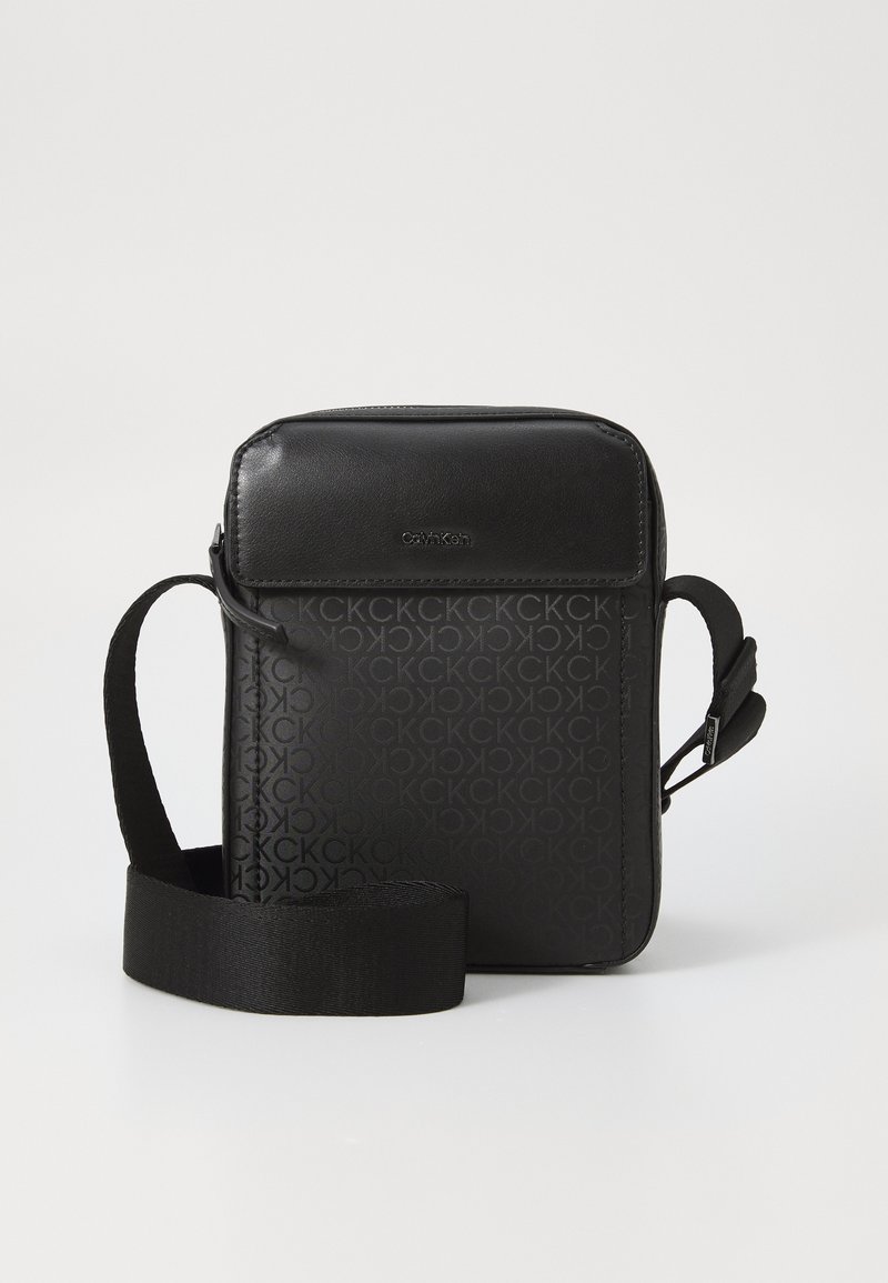Borsa a tracolla nera in materiale sintetico testurizzato, con motivo a logo ripetuto e tracolla regolabile. Pannello frontale liscio.