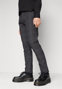 Pantalon à carreaux gris coupe slim, en tissu texturé. Associé à des chaussures noires à lacets avec une semelle épaisse et soulignée.